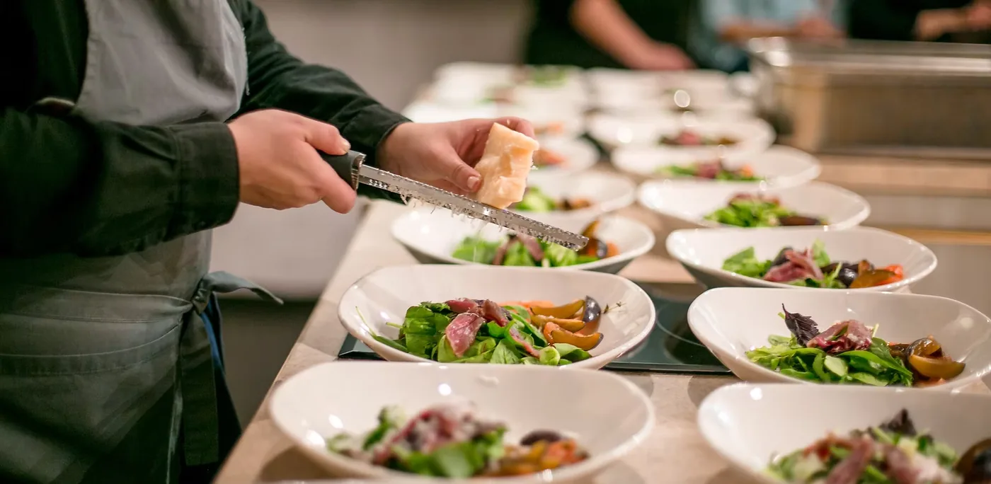 A cook plating rows of fresh salads in a kitchen