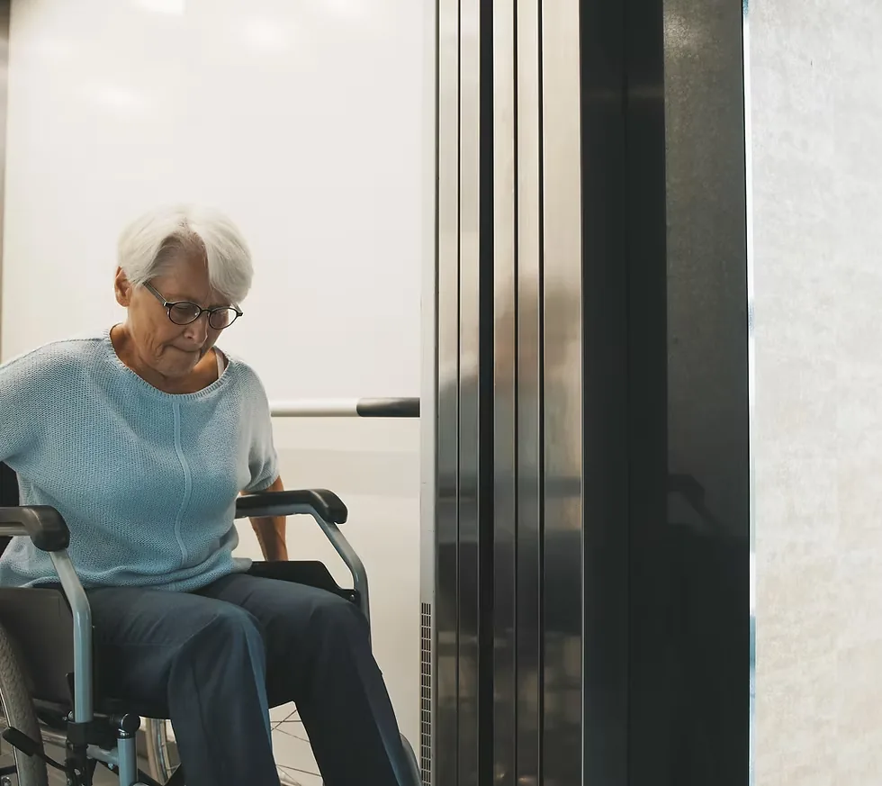 An older woman in a wheelchair waiting by an elevator